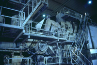 A l'intérieur de l'usine, d'énormes machines fabriquent, en continue, de grosses bobines de papier. La nouvelle feuille passe ensuite entre de très nombreux rouleaux qui la pressent et la chauffent.